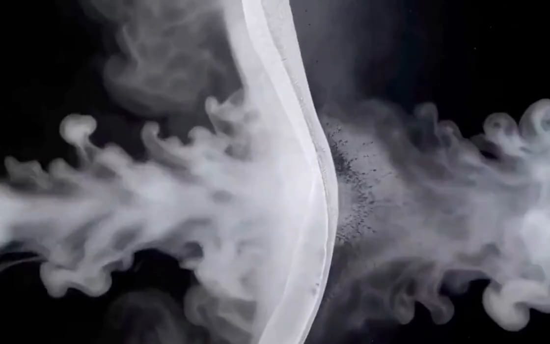 A cloud of white vapour with fine dark particles caught in it, against black.